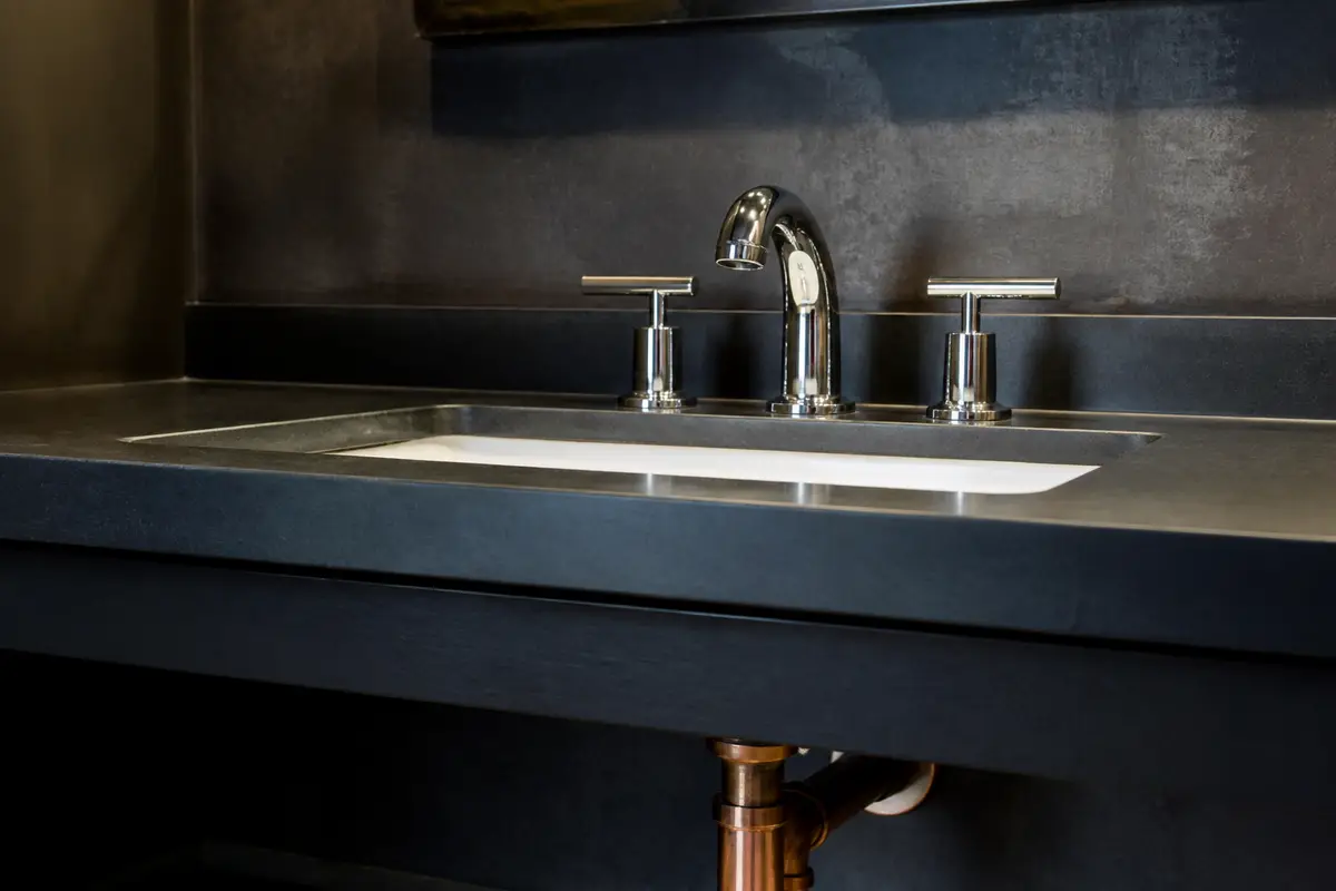 Chrome bathroom faucet on a dark vanity with supply lines below